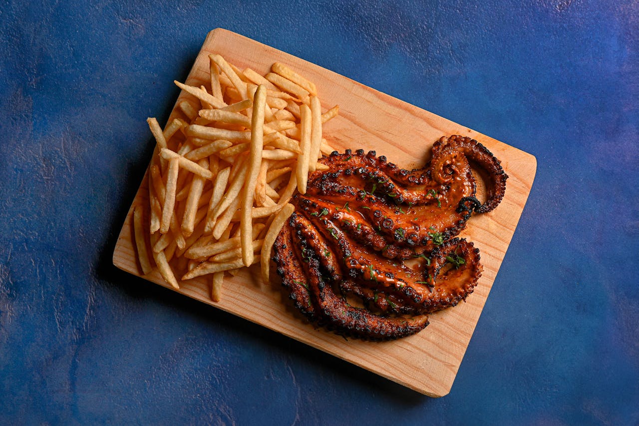 project-01-d Delicious grilled octopus served with crispy French fries on a wooden board, perfect for seafood lovers.