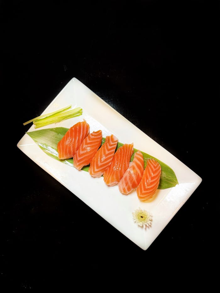 project-03-c Delicious slices of fresh salmon sashimi on a white platter, garnished with greens and a flower.