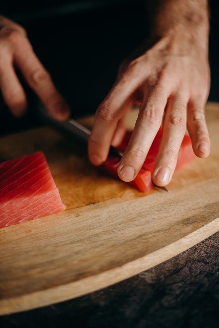 project-01-c Hands expertly slicing fresh tuna on a wooden board, showcasing precision and culinary skill.