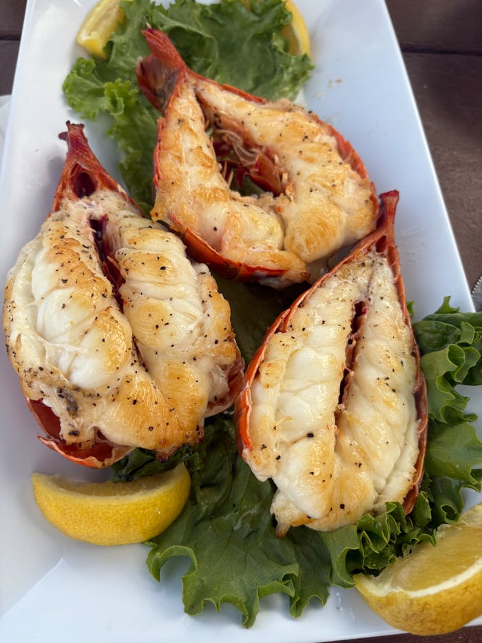 projects-header Delicious grilled lobster tails served with lemon slices and fresh greens, perfect for a seafood feast.