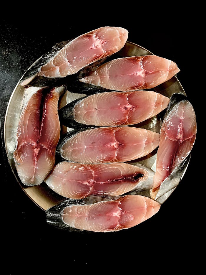 project-03-b Top view of fresh raw fish slices arranged on a stainless steel plate with a black background.